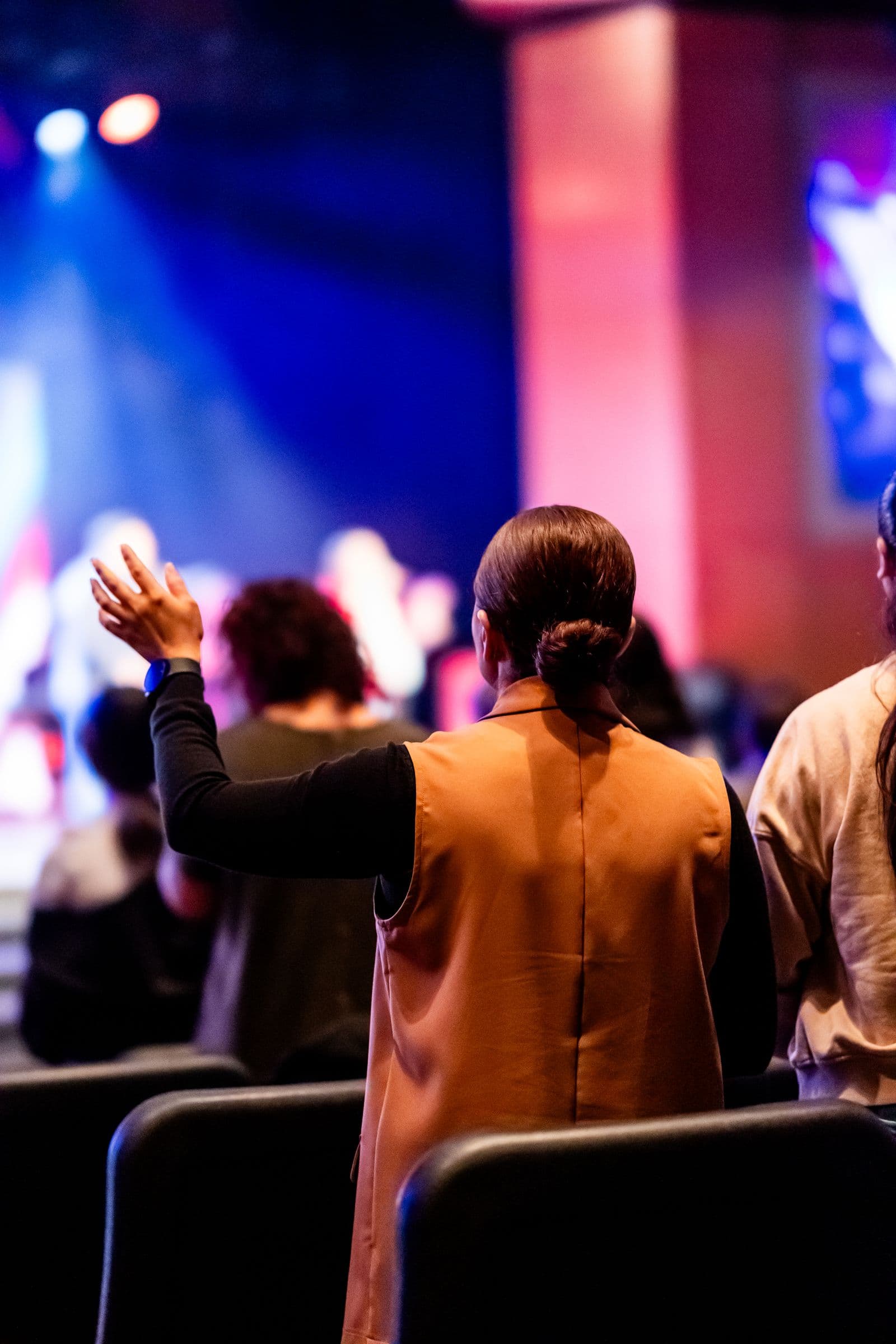 Congregation participating in a live worship event under colorful stage lighting